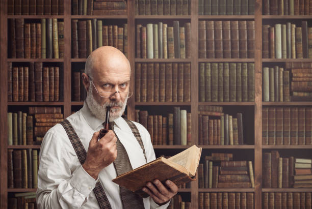 Academic professor in the library holding a book Senior academic professor reading an old book in the library, knowledge, learning and education concept philosopher stock pictures, royalty-free photos & images