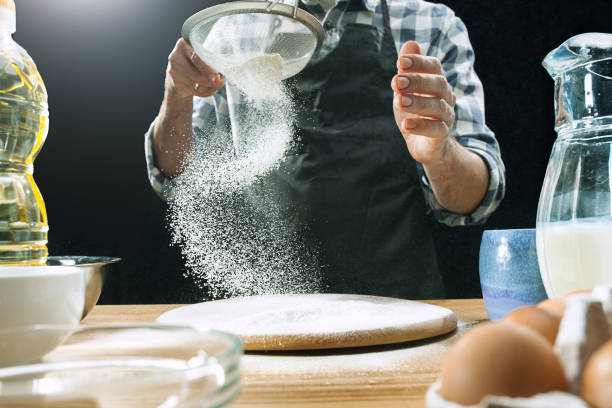 istock Professional male cook sprinkles dough with flour, preapares or bakes bread at kitchen table 1083622090