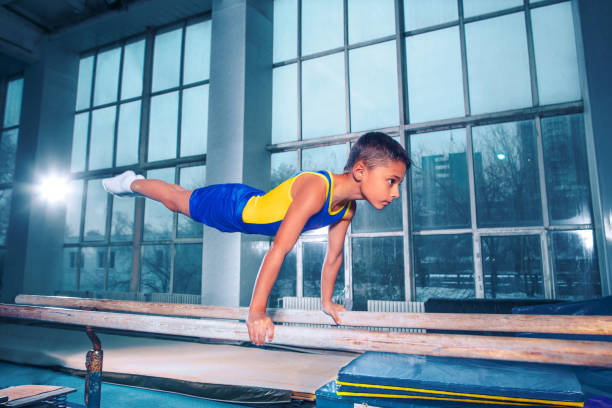 beau garçon est engagé en gymnastique sportive sur une barres parallèles - male body sport exercising photos et images de collection