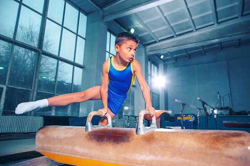 The sportsman performing difficult gymnastic exercise at gym. The sport, exercise, gymnast, health, training, athlete concept. Caucasian fit little boy