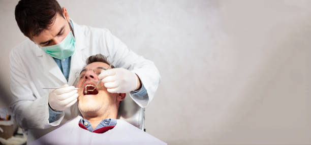 joven masculino dentista sosteniendo un espejo del diente y selección dental, realizar examen dental en un paciente varón maduro en clínica dental. imagen de proporción amplia con espacio de copia en el lado derecho - medical exam dental hygiene caucasian mask fotografías e imágenes de stock