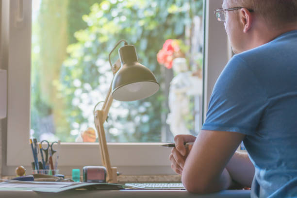 Man looks out of the window in his home office home office desk lamp photos stock pictures, royalty-free photos & images