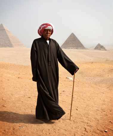 Mature bedouin is posing in desert behind pyramids in Egypt.