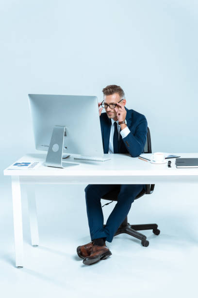 istock handsome businessman wearing glasses and looking at computer at table isolated on white 1083657562
