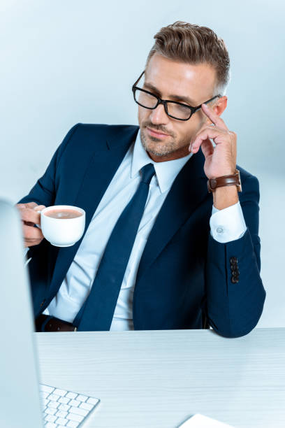 istock handsome businessman holding cup of coffee and looking at computer isolated on white 1083657576