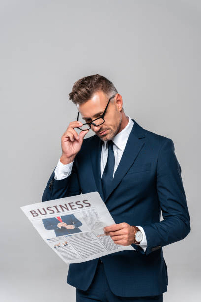 istock handsome businessman touching glasses and reading newspaper isolated on white 1083657672
