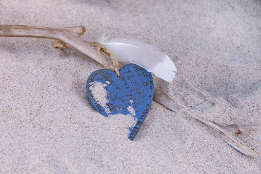Blue wooden heart and white feather on a piece of driftwood in the sand