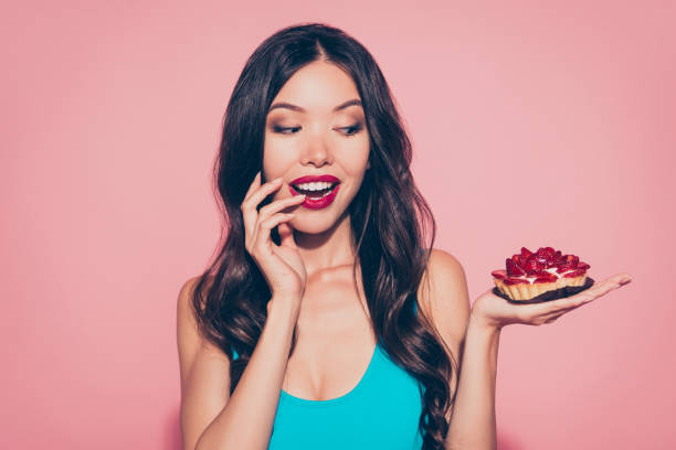 Close-up portrait of nice positive wondered lovely adorable char Close-up portrait of nice positive wondered lovely adorable charming attractive wavy-haired lady showing holding on palm sugary dessert bakery red lips white teeth isolated over pink pastel background cake models stock pictures, royalty-free photos & images