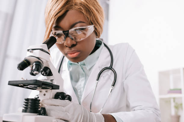 istock selective focus of female african american scientist looking through microscope 1083660678
