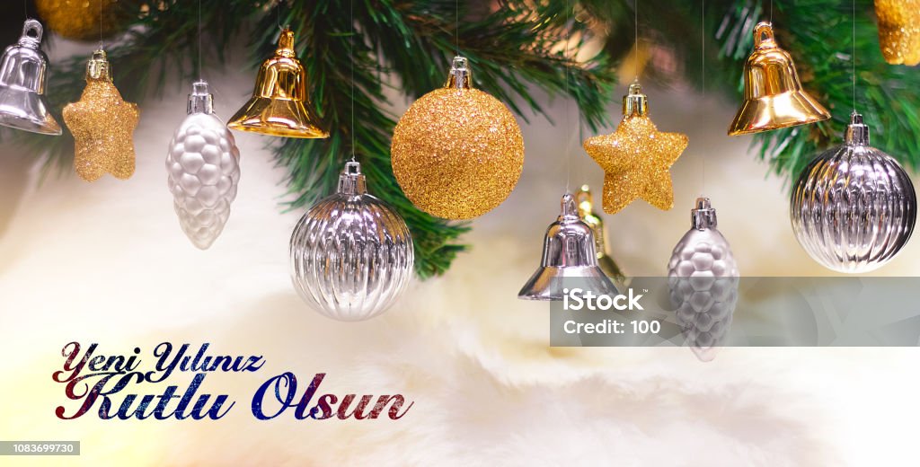 Shiny gold and silver christmas balls, stars and bells on white with pine tree. Yeni yiliniz kutlu olsun means happy new year Shiny gold and silver christmas balls, stars and bells on white with pine tree. Yeni yiliniz kutlu olsun means happy new year. Bell Stock Photo