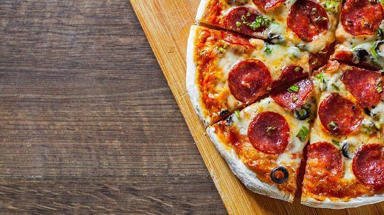 Pizza with Mozzarella cheese, pepperoni, tomato, pepper, olive, salami. Italian pizza on wooden table background