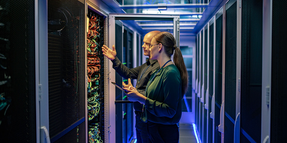 Side view of a man and a woman talking about a server in a data center while looking at it's network connection cables.