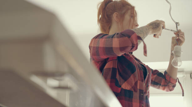 istock Woman in new home changing light bulb 1083730540