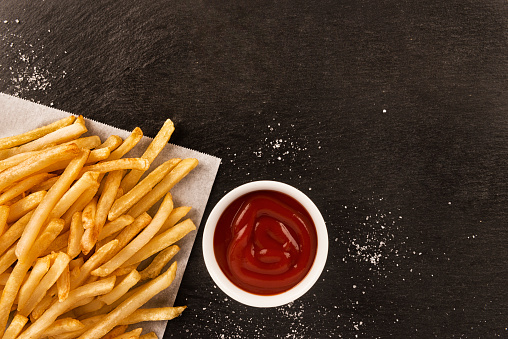 French fries with ketchup on dark background, directly above.