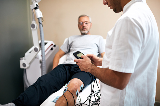 Physical therapist preparing for TENS therapy on senior man