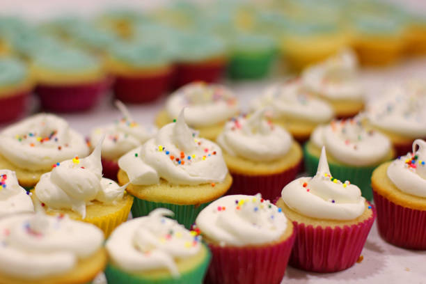 istock Mini vanilla cupcakes with white icing and sprinkles in paper wrappers. 1083754438
