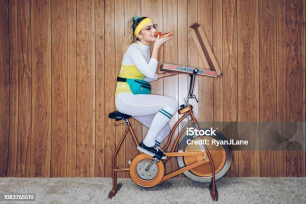 Retro Style Exercise Bike Woman Eighties Era Eating Pizza Stock Photo - Download Image Now