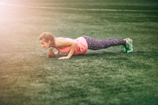 Fit woman in bright sports clothes to do burpees on the green grass stock photo