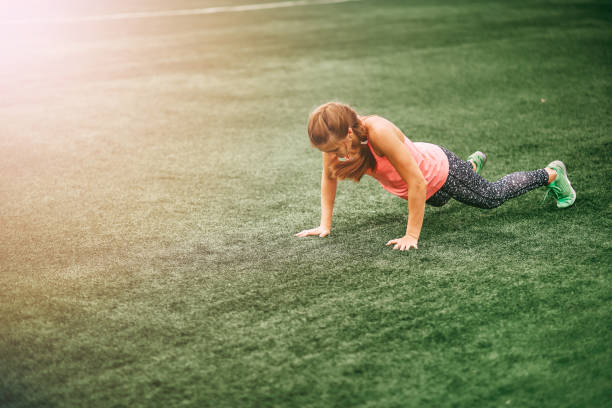 Fit woman in bright sports clothes to do burpees on the green grass stock photo