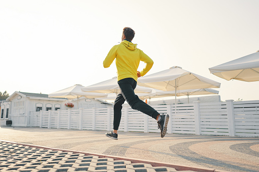 Full length shot of healthy young man running on the promenade in the morning. Male runner sprinting outdoors. Down angle