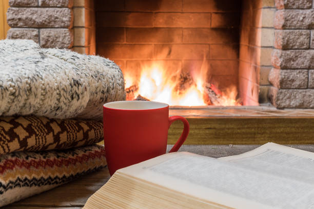 istock Cozy scene before fireplace with orange mug with tea, a book, wool things. 1083782340