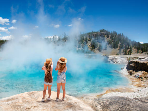 Girls relaxing and enjoying beautiful view on vacation hiking trip. Girls  relaxing and enjoying beautiful view of gazer on vacation hiking trip. Friends on hiking trip. Excelsior Geyser from the Midway Basin in Yellowstone National Park. Wyoming, USA midway geyser basin photos stock pictures, royalty-free photos & images