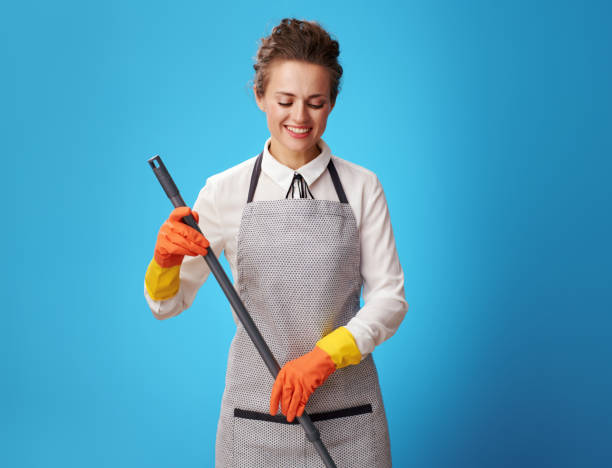 istock smiling young cleaning lady in apron on blue using mop 1083795480