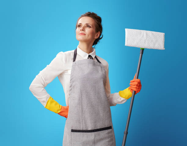 istock proud young housemaid in apron on blue with mop 1083796580