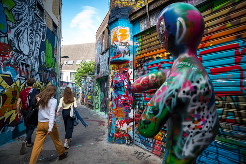 Three young people walk through the Werregarenstraatje, a narrow alley decorated with graffiti since 1995. Located in the center of Ghent, this alley has become a tourist attraction for some years. The works of art are changing every month, and from time to time the walls are painted white to facilitate the creation of new graffiti.