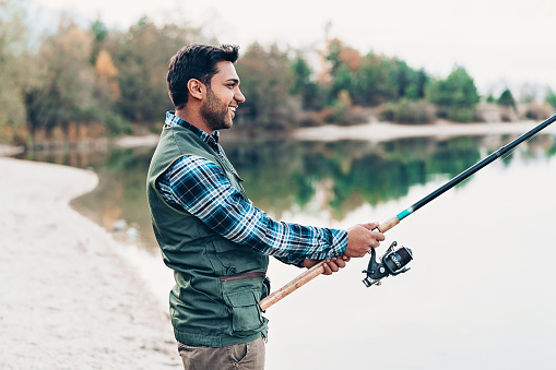 Smiling young man with fishing rod by the river