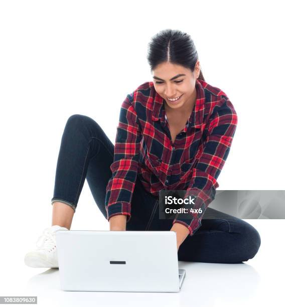 Beautiful Young Latino Female Sitting On Floor And Using Laptop Stock Photo - Download Image Now