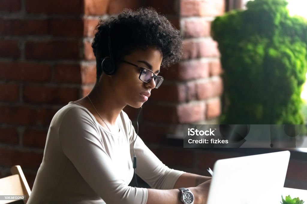 Konzentrierte sich afrikanische amerikanische Frau, die mit Kopfhörern mit laptop - Lizenzfrei Internet Stock-Foto