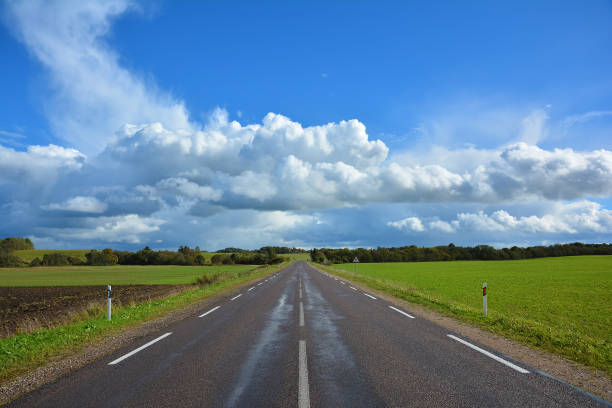 zweispurige asphaltierte landstraße, die hinter dem horizont liegt. landschaft mit blick auf nicht-städtische auffahrt, grün 

feld, bäume und blauer himmel mit weißen wolken. herbstlandschaft an einem sonnigen, klaren tag. - non urban scene nature rural scene outdoors stock-fotos und bilder