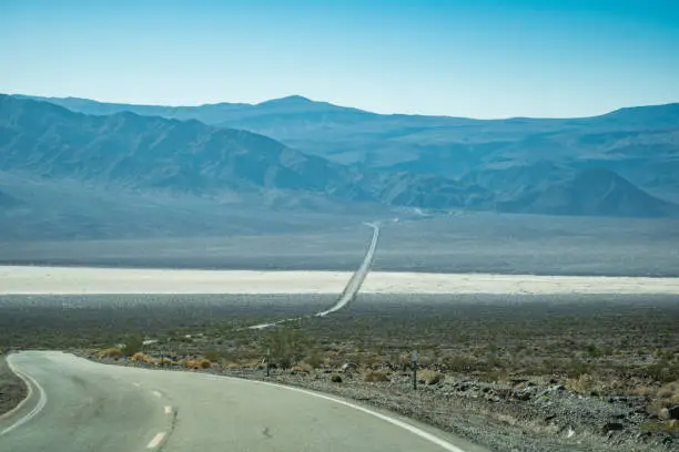 View from the endless road through Death Valley National Park (California State Route 190), with a view of the Sierra Nevada mountains in the background on a hazy sunny day