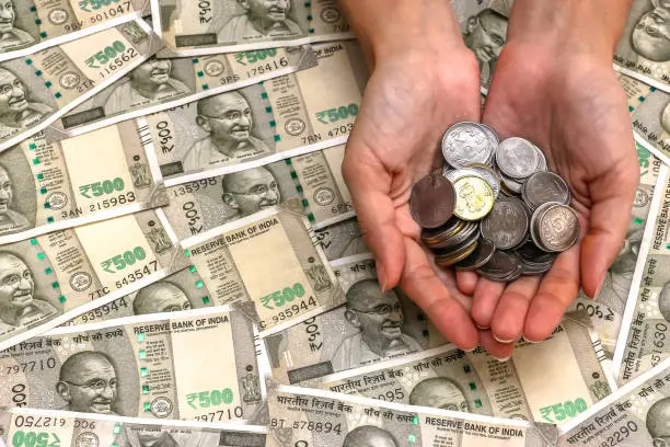Close up view of woman's hands with indian rupees coins. 500 rupee banknotes in background.