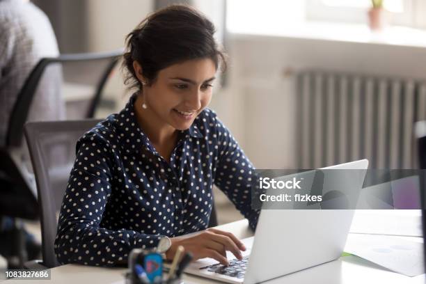 Smiling Indian Female Employee Using Laptop At Workplace Stock Photo - Download Image Now