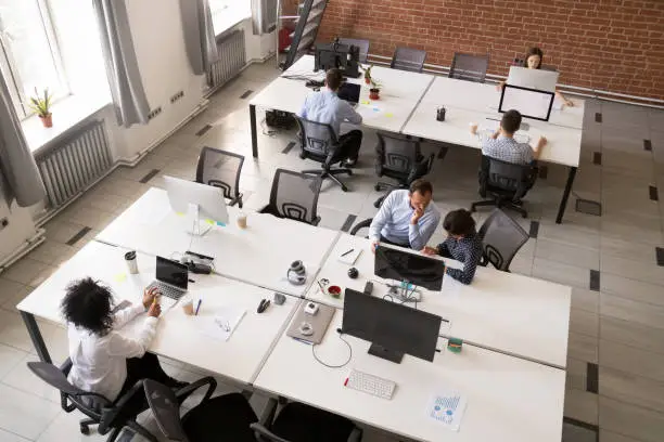 Employees working together in modern open office space, corporate group team employees using computers, talking, discuss project, colleagues in coworking, collaboration, teamwork concept, top view