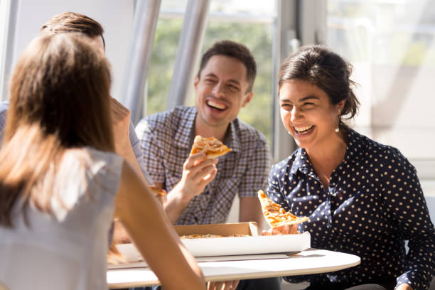 Indian woman laughing, eating pizza with colleagues in office Indian excited woman laughing at funny joke, eating pizza with diverse colleagues in office, happy multi-ethnic employees having fun together during lunch, enjoying good conversation, emotions indian woman laughing stock pictures, royalty-free photos & images