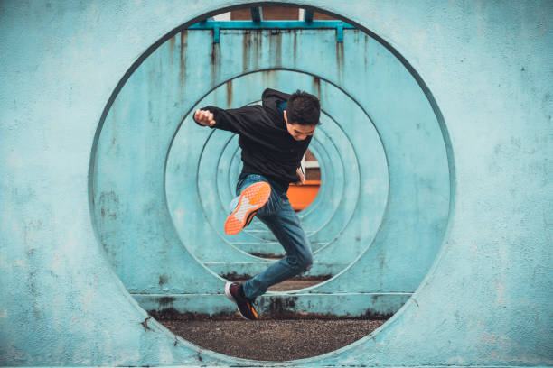 giovane uomo attivo asiatico in azione di salto e calci, cerchio looping parete sfondo. attività sportiva estrema, parkour corsa libera all'aperto o concetto di stile di vita sano - courage foto e immagini stock