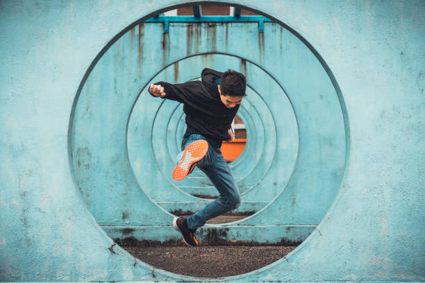 молодой азиатский активный человек в действии прыгает и пинает, кружит циклический фон стены. экстремальные виды спорта, паркур на открыто� - улица фотографии стоковые фото и изображения