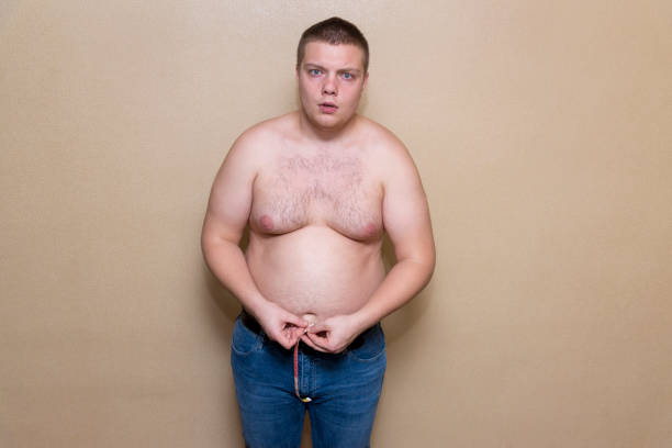 A man measures his fat belly with a meter A young man measures his fat belly with a meter fat guy no shirt stock pictures, royalty-free photos & images