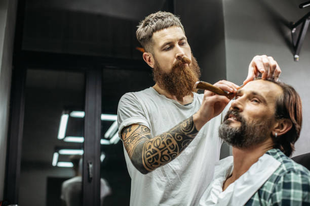 istock Close up of professional barber working with his client and using straight razor 1083853302