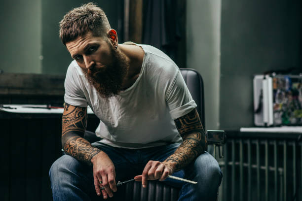 Serious barber frowning while holding straight razor