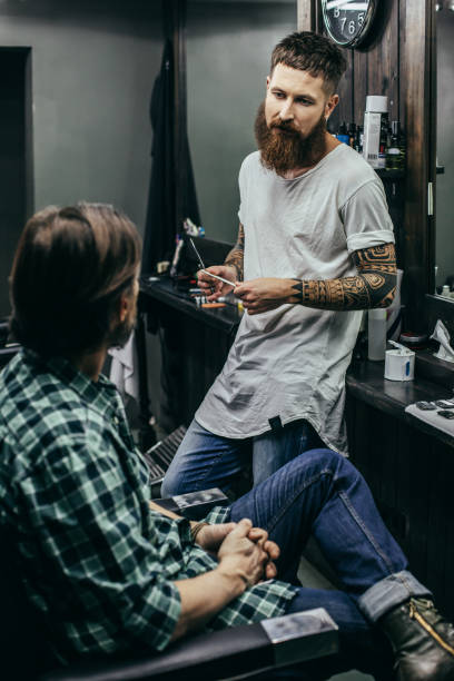 istock Thoughtful barber looking at his client while sitting in front of him 1083857448