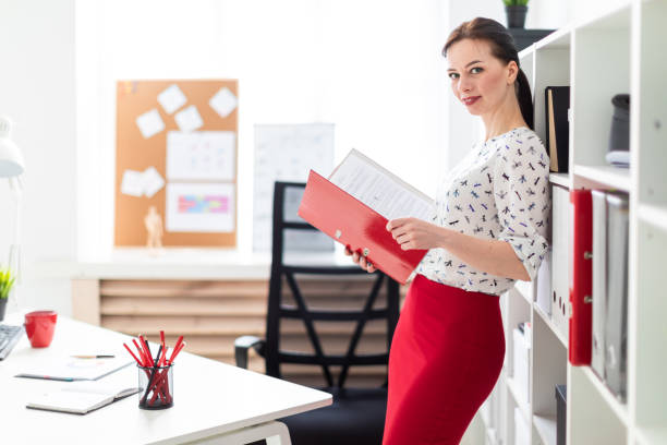 istock A young girl standing in the office and holding a red folder with documents. 1083896408