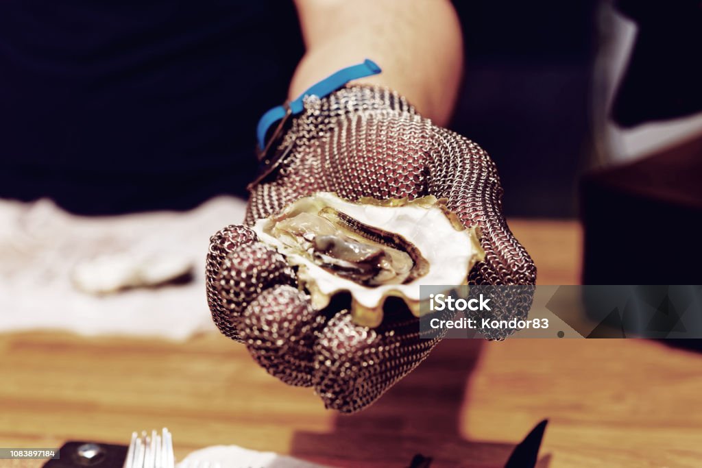 Chef is shoving open oyster, toned Chef is shoving open oyster in armour gloved hand, toned image Armored Clothing Stock Photo