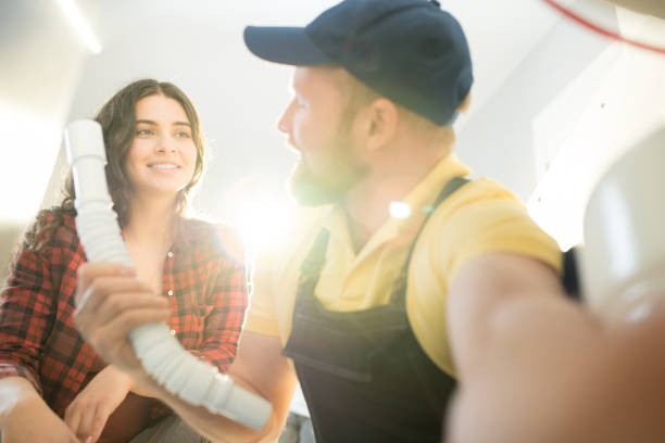 Plumber changing sink pipe Smiling handsome young plumber in cap holding sink pipe and showing it to home owner while changing pipe clogged drain stock pictures, royalty-free photos & images