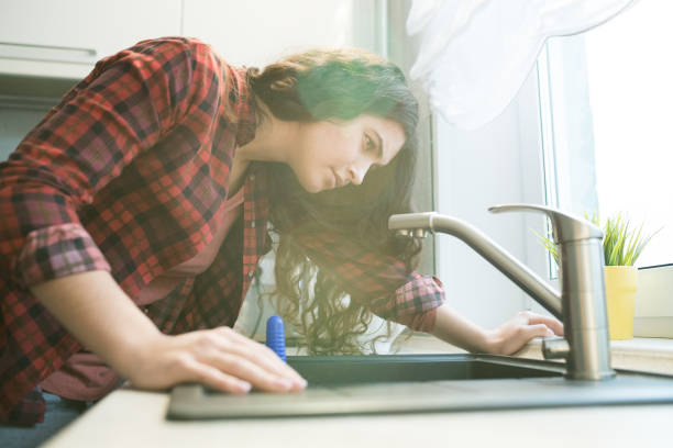 Problem with faucet in kitchen Serious concentrated young woman in checkered shirt checking faucet while having problem with dropping faucet in kitchen leaking stock pictures, royalty-free photos & images