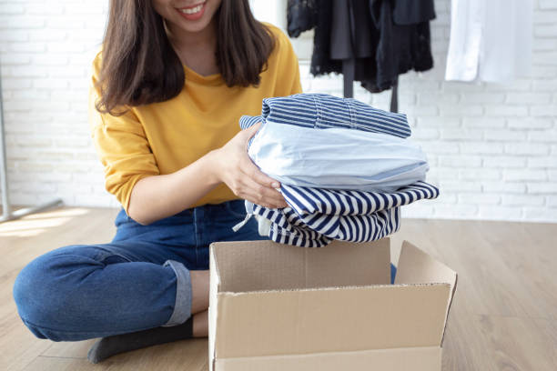 Woman holding Clothes with Donate Box In her room, Donation Concept. stock photo