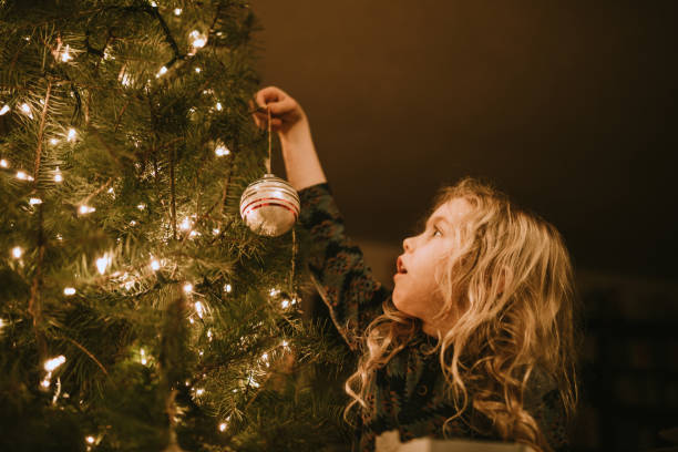 little girl decorating christmas tree with ornaments - christmas tree fotos imagens e fotografias de stock